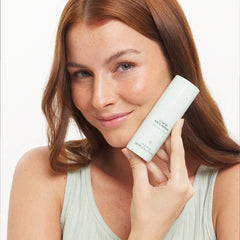 Woman holding a skincare product with a plain background