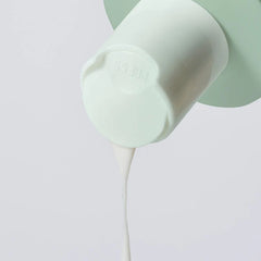 Light green silicone bottle with a white stream on cleanser pouring out on a light gray background